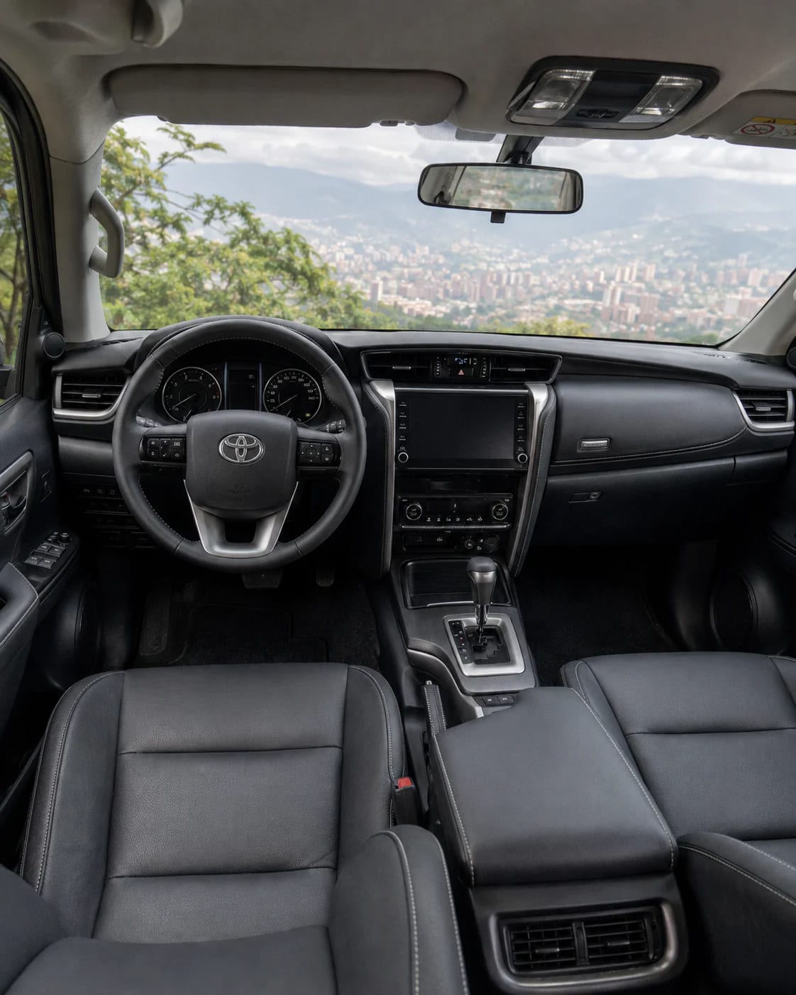 Interior de la Toyota Fortuner desde la segunda fila: tablero, pantalla y asientos delanteros en cuero negro.