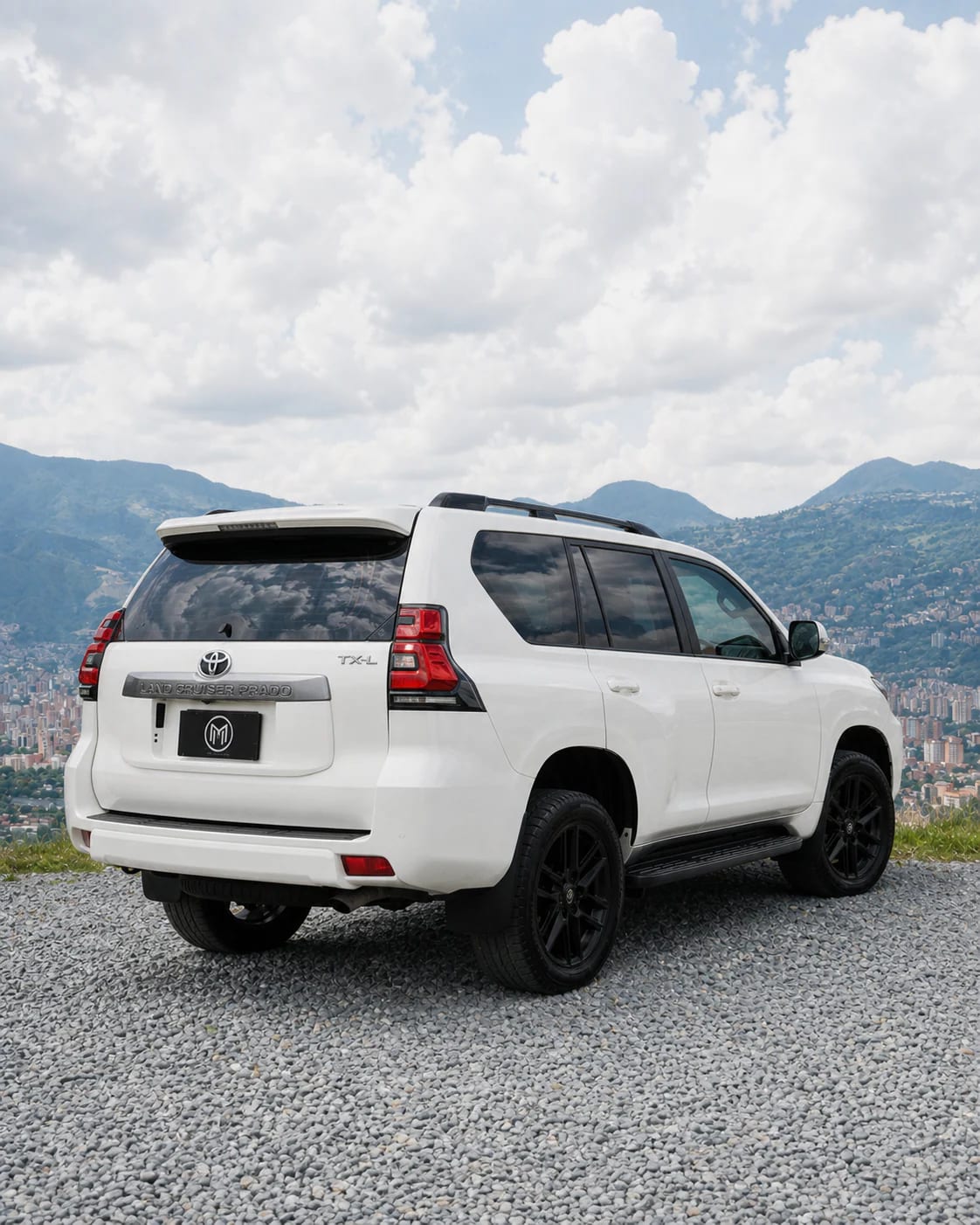 Toyota Prado blanca de tres cuartos traseros, con el portón y las luces a la vista y Medellín al fondo.