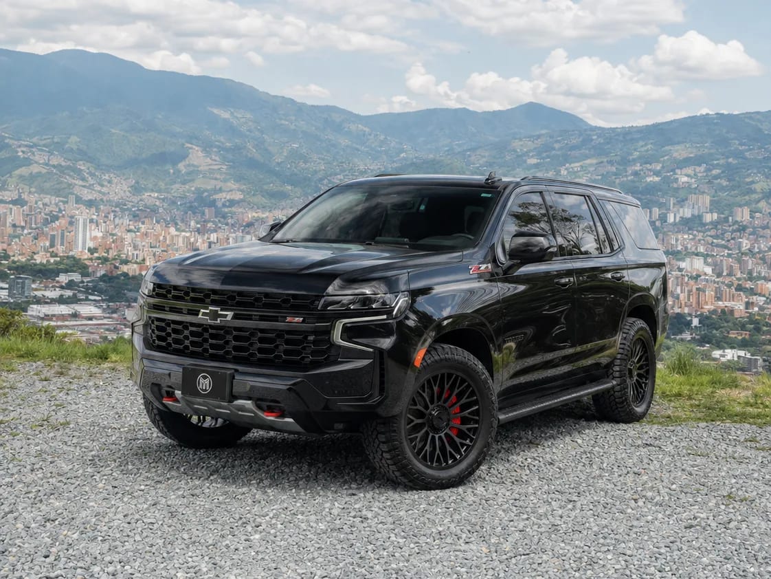 Black Chevrolet Tahoe with dark wheels, front three-quarter view, at a lookout with Medellín and the mountains behind.