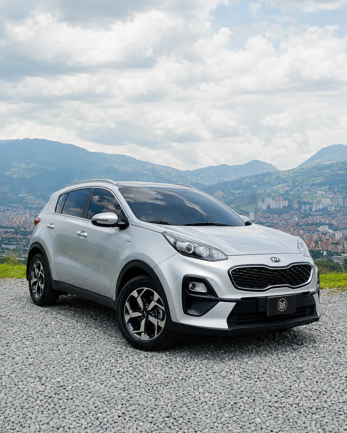 Silver Kia Sportage, front three-quarter view, at a lookout with Medellín behind.