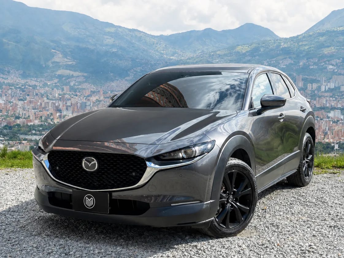 Graphite grey Mazda CX-30 with black wheels, front three-quarter view, at a lookout with Medellín behind.