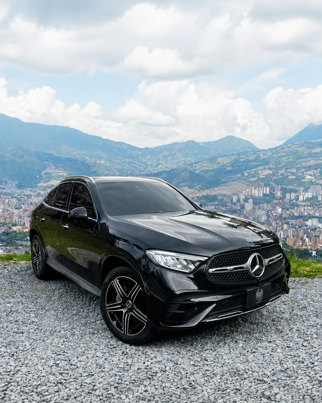Black Mercedes-Benz GLC 300 with two-tone wheels, front three-quarter view, at a lookout with Medellín behind.
