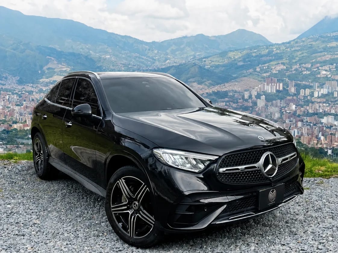 Black Mercedes-Benz GLC 300 with two-tone wheels, front three-quarter view, at a lookout with Medellín behind.