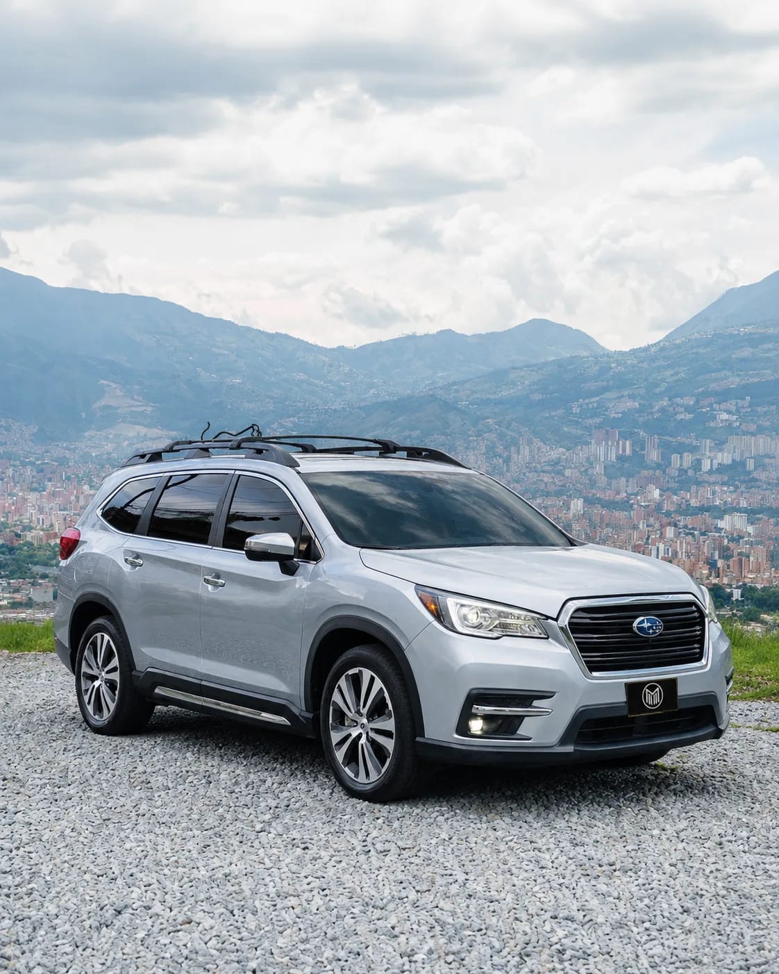 Silver Subaru Evoltis with roof rails, front three-quarter view, at a lookout with Medellín behind.