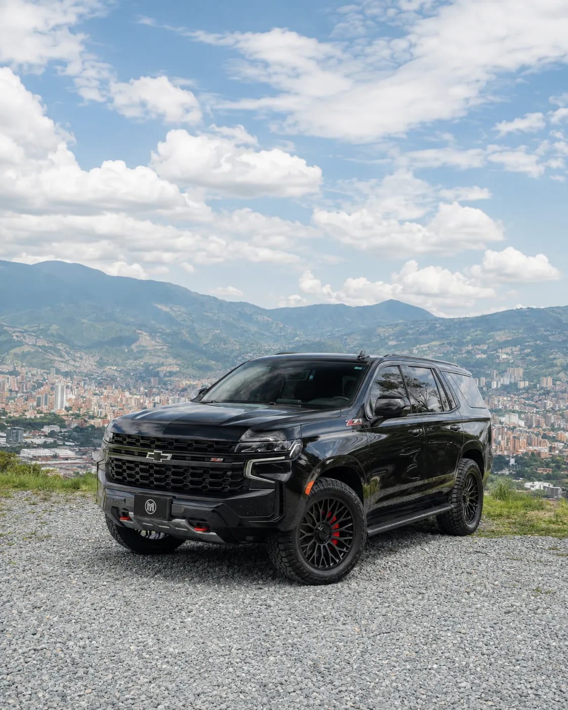 Chevrolet Tahoe negra con rines oscuros, de tres cuartos frontal, sobre un mirador con Medellín y la cordillera al fondo.