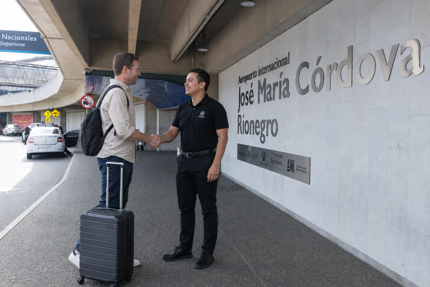 A Majestic adviser in a black shirt shakes hands with a traveller carrying a suitcase at the entrance of José María Córdova International Airport, in Rionegro.
